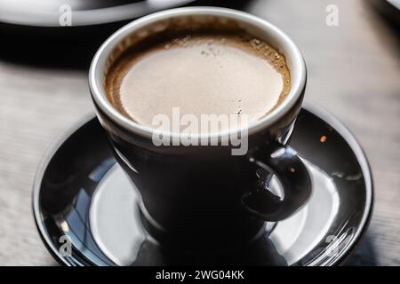 Traditional espresso coffee in a black cup on a table in a cafe. Stock Photo