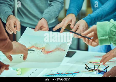 Individuals examining and discussing a complex data visualization sheet among other graphs. Collages working with analytical graphs Stock Photo