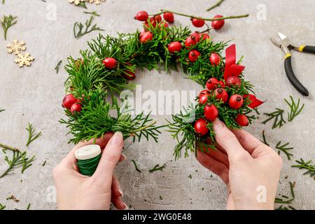 Florist at work: How to make traditional christmas door wreath with thuja twigs and wild rose fruits. Step by step, tutorial. Stock Photo