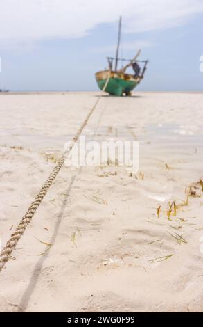 Rusty boat anchored at the beach. Tropical low tide landscape with sailboat. Boat with anchored rope, selected focus. Nautical vessel on beach, Africa Stock Photo