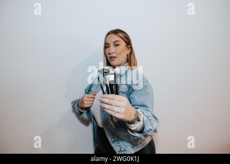 Girl with short blonde hair, jean jacket, showcasing makeup brushes Stock Photo