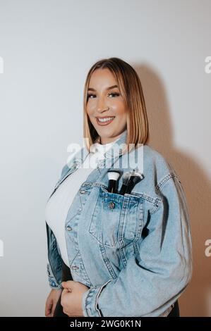 Girl with short blonde hair, jean jacket, showcasing makeup brushes Stock Photo