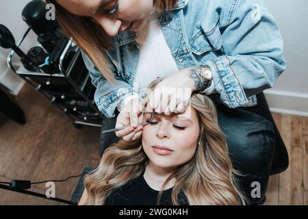 Girl with short blonde hair applies eyelashes to a client laying down Stock Photo