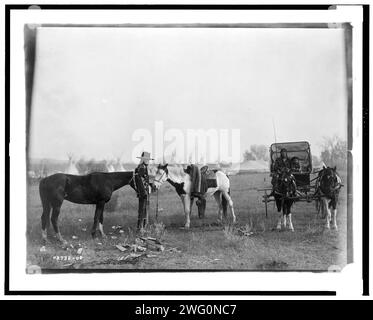 High Medicine Rock, Crow Indian with two horses at left, Her Horse Kills with child in buggy at right, tepees and circus type tent in background, Montana, c1908. Stock Photo