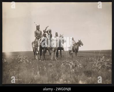 The war party, 1905. Photograph shows a group of Crow Indians on horseback. Chief, in middle, wearing headdress. Stock Photo