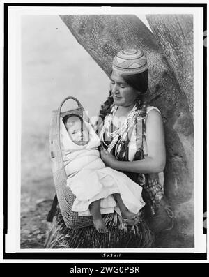 Hupa mother, three-quarter length portrait, seated, facing left, holding baby, c1923. Stock Photo