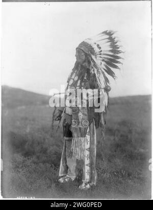 High Hawk, c1907. High Hawk, standing, facing left, in ceremonial dress, war bonnet and holding a coup stick. Stock Photo