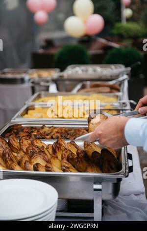 A person in front of a buffet table with food trays plates and bowls Stock Photo