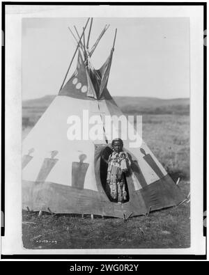 Crow Chief's Daughter, c1910. Piegan girl standing in doorway of tepee, wearing beaded buckskin dress, Montana. Stock Photo