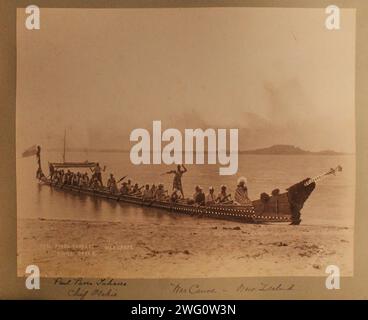 Maori canoe. New Zealand, Thirty-three men sit in a long canoe next to a beach. Man in front, probably the 'chief,' wears cloak around his shoulders. Others wear combinations attire, most with feathers in their hair. Distant shore in background. From Charles Appleton Longfellow's trip to New Zealand in 1891. Stock Photo