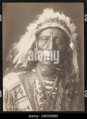 Jack Red Cloud, 1907. Photograph shows head-and-shoulders portrait of Jack Red Cloud, standing, wearing full headdress, traditional clothing, and medallion, facing front. Stock Photo