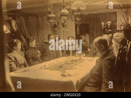 Captains, their wives, and two female tourists sitting around a table aboard ship, Dutch Harbor, Alaska, (1897?).. Stock Photo