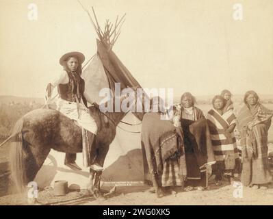 A pretty group at an Indian tent, 1891. Four Lakota women standing, three holding infants in cradleboards, and a Lakota man on horseback, in front of a tipi, probably on or near Pine Ridge Reservation. Stock Photo