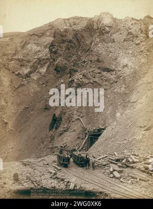 Open cut in the great Homestake mine, at Lead City, Dak, 1888. Distant view of mine entrance; four men posed on or near three mining cars on tracks. Stock Photo