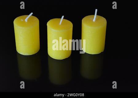 Home furnishings, yellow bright candles placed on black glossy background. Stock Photo