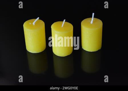 Home furnishings, yellow bright candles placed on black glossy background. Stock Photo