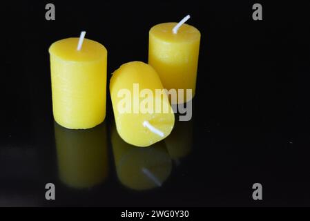 Home furnishings, yellow bright candles placed on black glossy background. Stock Photo