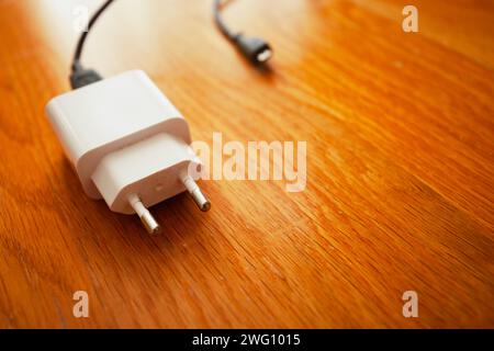 A white smartphone charger lies on the wooden brown floor Stock Photo