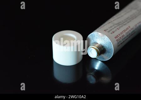 Cosmetics, white anti-inflammation cream in a white metal tube placed on a black glossy background. Stock Photo