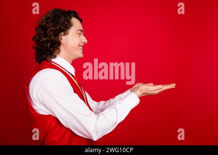 Side profile photo of young teenage gentleman guy curly hair gentleman working like waiter in restaurant isolated on red color background Stock Photo