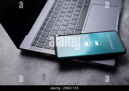 Contact us or customer support hotline concept. Smartphone resting on laptop with contact icons on screen. Email, address, live chat, call. Stock Photo