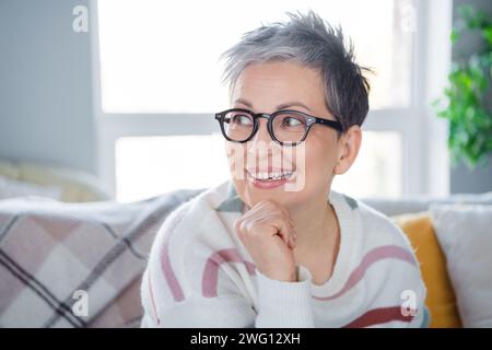 Photo of pretty thoughtful woman dressed striped sweater eyewear having rest couch indoors house home room Stock Photo