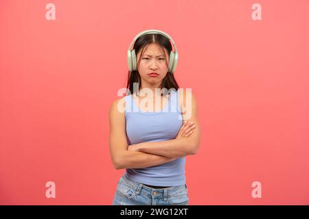 Young serious Chinese woman posing on pink background listening to music. Stock Photo