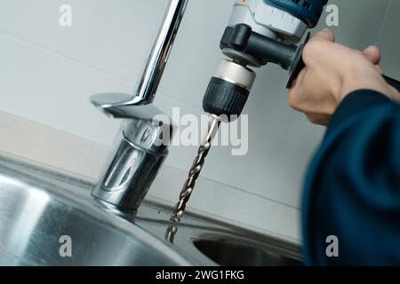 closeup of a caucasian man, wearing blue overalls, drilling a hole in a metal kitchen sink with a drill Stock Photo