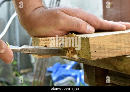 A close-up of the carpenter's hands, who removes excess pieces from the board with a chisel. Stock Photo