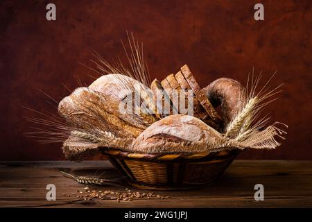 In the wicker basket different types of bread, wholemeal with seeds and cereals and a few ears of wheat. Still life Stock Photo