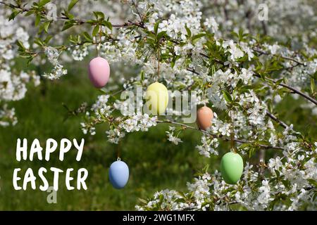 Greeting card with wishes of Happy Easter. branches of cherry blossoms in garden are decorated with decorative Easter eggs. Holiday concept. Religious Stock Photo