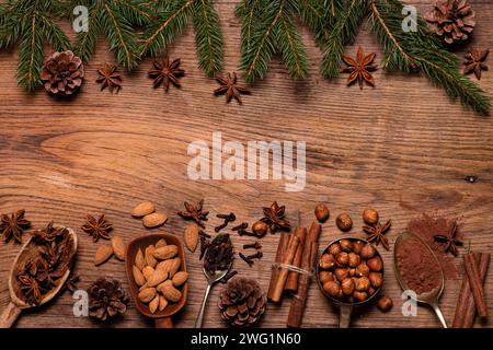 Top view, on a textured wooden background, pine branches with pine cones, various spices and dried fruits. Blank space for your text. Christmas scene. Stock Photo