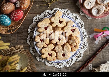 Homemade Linzer cookies in the shape of bunnies, chicken and four leaf clover, with Easter eggs in the background Stock Photo