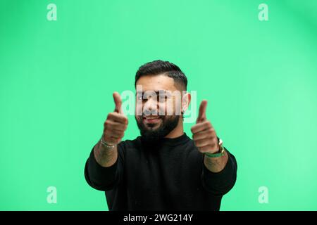 A man, close-up, on a green background, shows his thumbs up Stock Photo