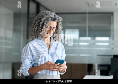 Smiling mature professional business woman entrepreneur using phone in office. Stock Photo
