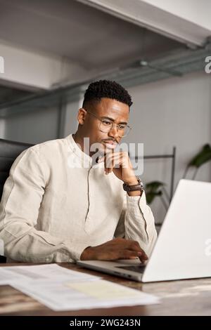 Busy African business man investor thinking working on laptop, vertical. Stock Photo