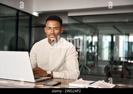 Confident professional African business man looking at camera using computer. Stock Photo
