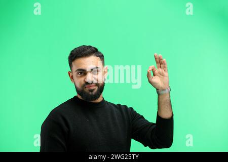 A man, close-up, on a green background, shows an ok sign Stock Photo