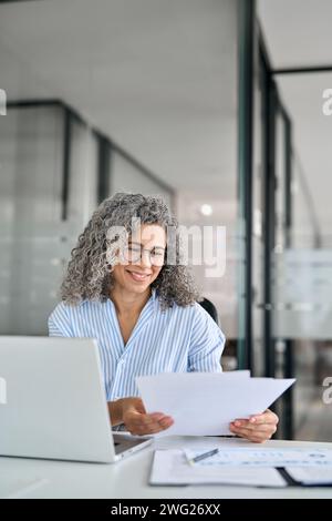 Busy mature business woman working in office with laptop and documents. Stock Photo