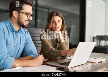 Female manager talking to male employee working on computer at office meeting. Stock Photo