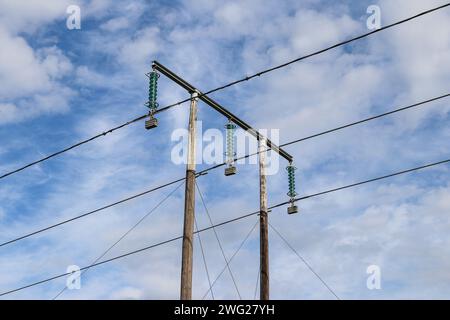 Three electrical high voltage cables on a pole with blue sky and clouds in the background Stock Photo