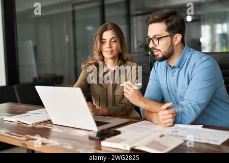 Two busy colleagues working together talking using laptop in office. Stock Photo
