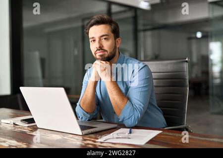 Young business man sitting at work desk in office with laptop, portrait. Stock Photo