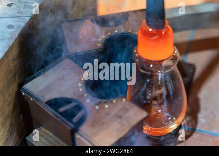 The process of glass making. Glassblower use wooden form for shaping the red melted glass Stock Photo