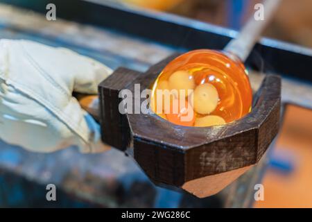 The process of glass making. Glass blower shaping a bubble of melted glass. Glassblower use wet wooden form for shaping the red melted glass Stock Photo