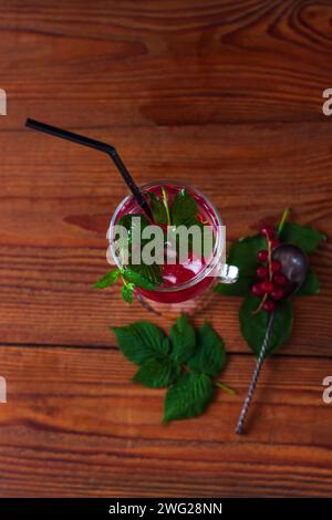 Summer red currant tea in a glass on dark brown wooden background. Cold fruit trendy cocktail. Tasty iced juice with fresh green leaves. Seasonal vita Stock Photo