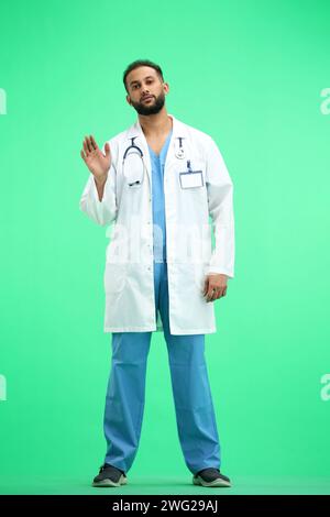The doctor, in full height, on a green background, waving his hand Stock Photo