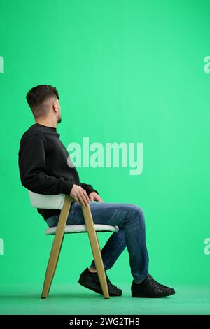 A man, on a green background, sitting on a chair Stock Photo