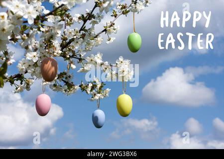 Greeting card with wishes of Happy Easter. branches of cherry blossoms are decorated with Easter eggs against blue sky. Holiday concept. Religious hol Stock Photo