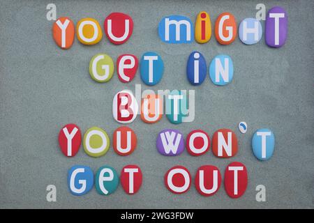 You might get in but you won t get out, creative advice composed with hand painted multi colored stone letters over green sand Stock Photo